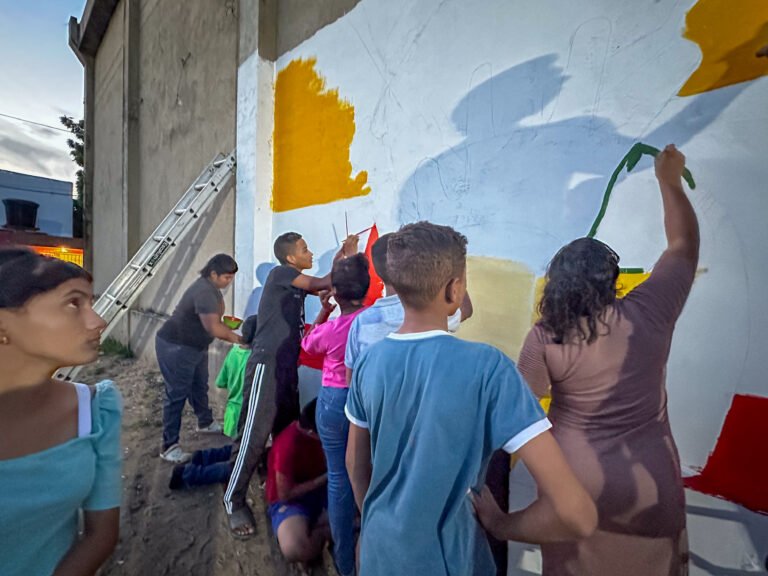 Jornada de muralismo en el barrio Hugo Zúñiga: Jóvenes líderes y habitantes trabajan en conjunto para pintar el mural Iluminando Nuestros Sueños, que refleja la identidad y la historia de su comunidad, fomentando el sentido de pertenencia y la cohesión social.